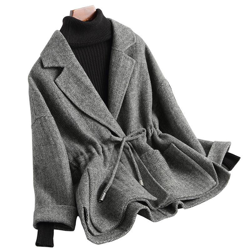 Gray herringbone belted jacket with wide lapels over black ribbed turtleneck sweater