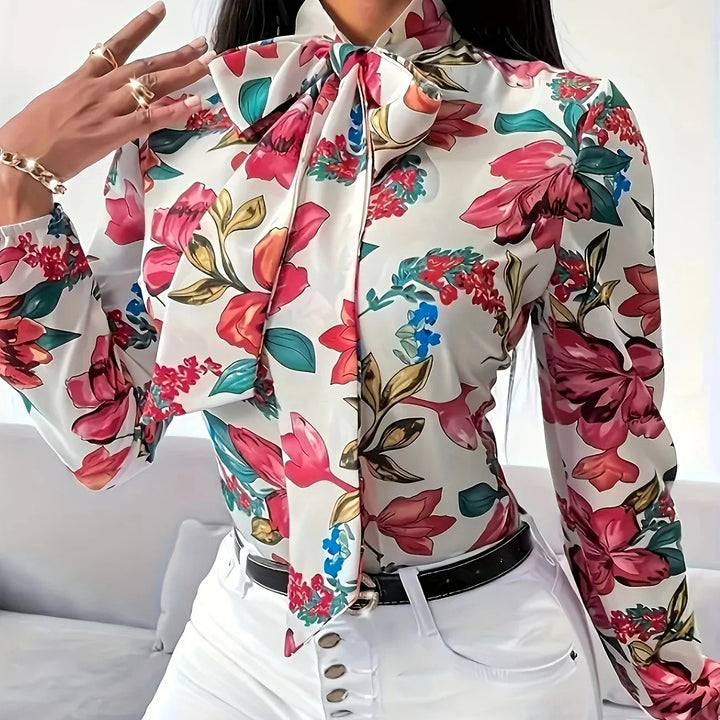 Woman wearing a floral print blouse with a large bow tie and white high-waisted pants