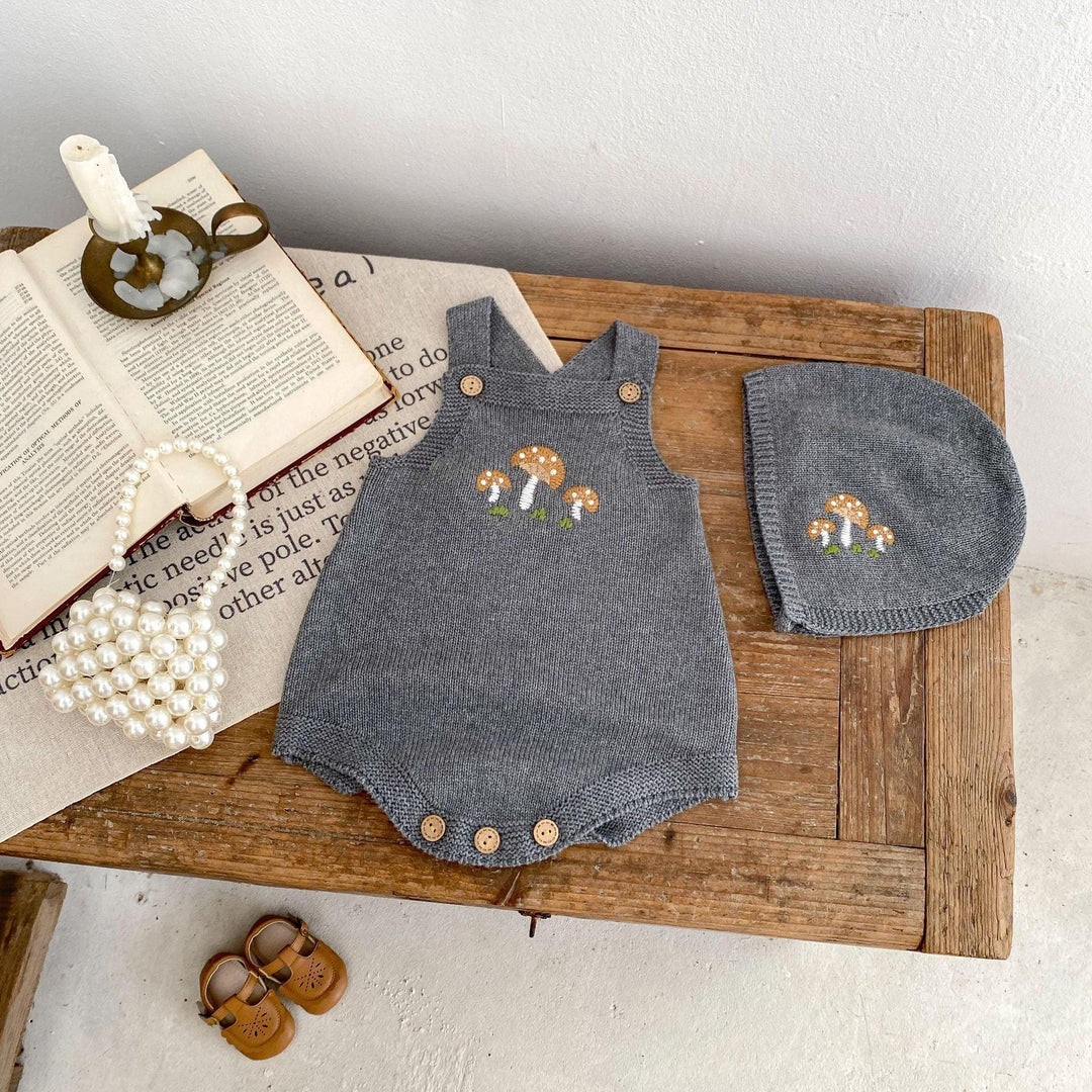 Grey knitted baby romper and matching hat with mushroom embroidery on wooden table