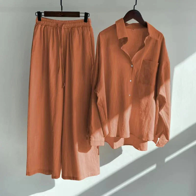 Rust orange loose-fit pants and long-sleeve button-up shirt hanging on wooden hangers against white wall