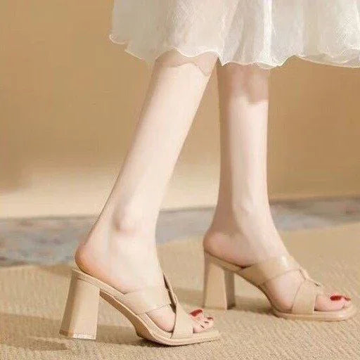 Woman wearing beige high-heeled mules with square open toes on a beige carpet