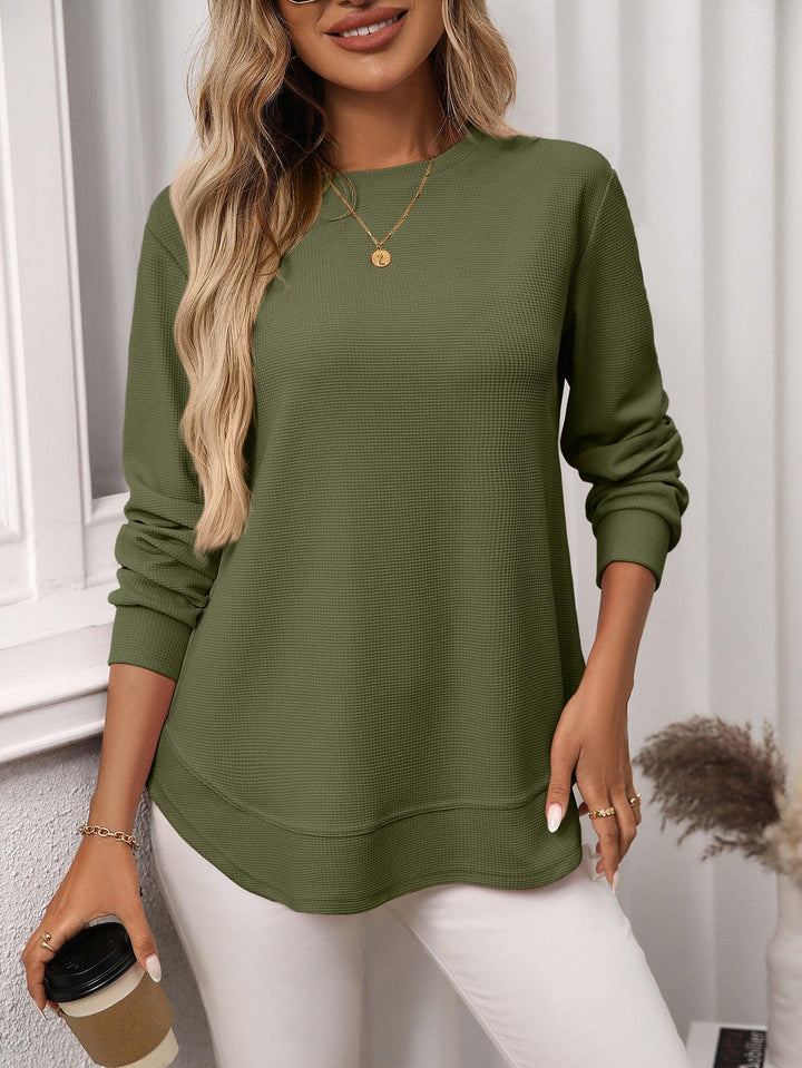 Woman wearing olive green long sleeve waffle knit top with white pants holding coffee cup
