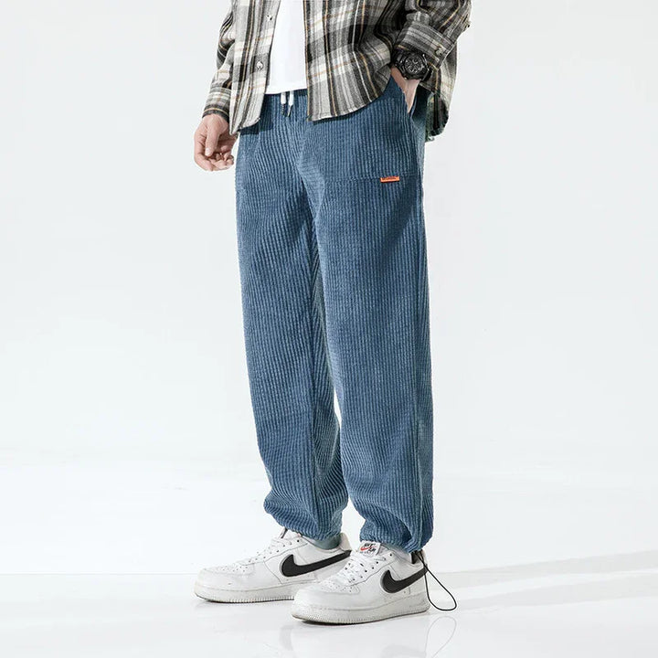 Man wearing blue corduroy pants with elastic cuffs and white Nike sneakers in casual outfit