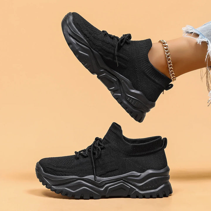 Black chunky knit sock sneakers with rugged soles worn with gold anklet and ripped jeans