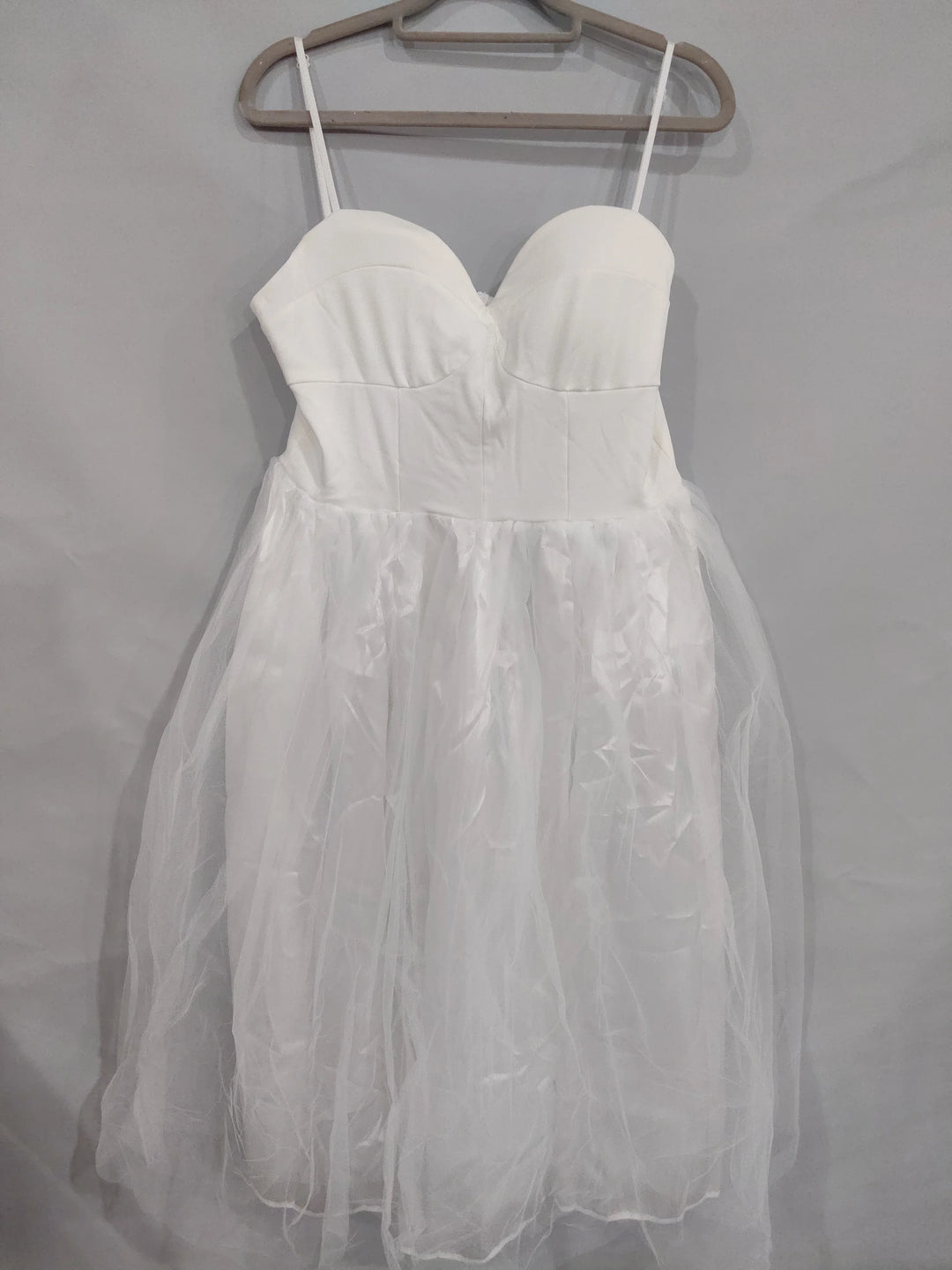 White strapless dress with sweetheart neckline and tulle skirt hanging on beige hanger