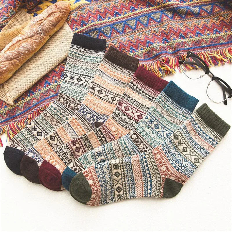 Set of colorful patterned wool socks on a white surface with a baguette, woven blanket, and eyeglasses