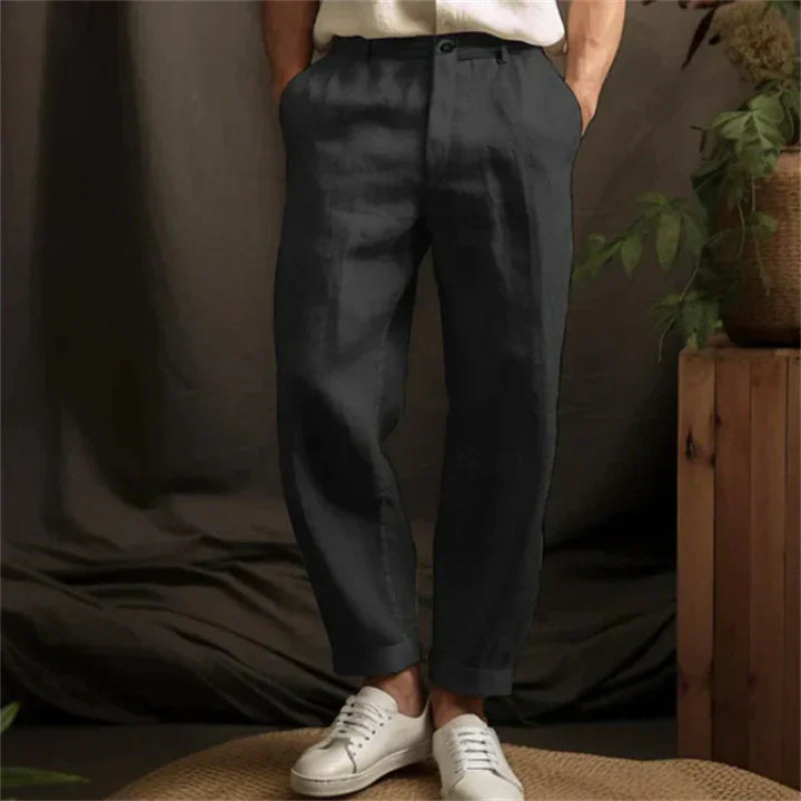 Man wearing black casual linen pants with white sneakers against dark fabric backdrop