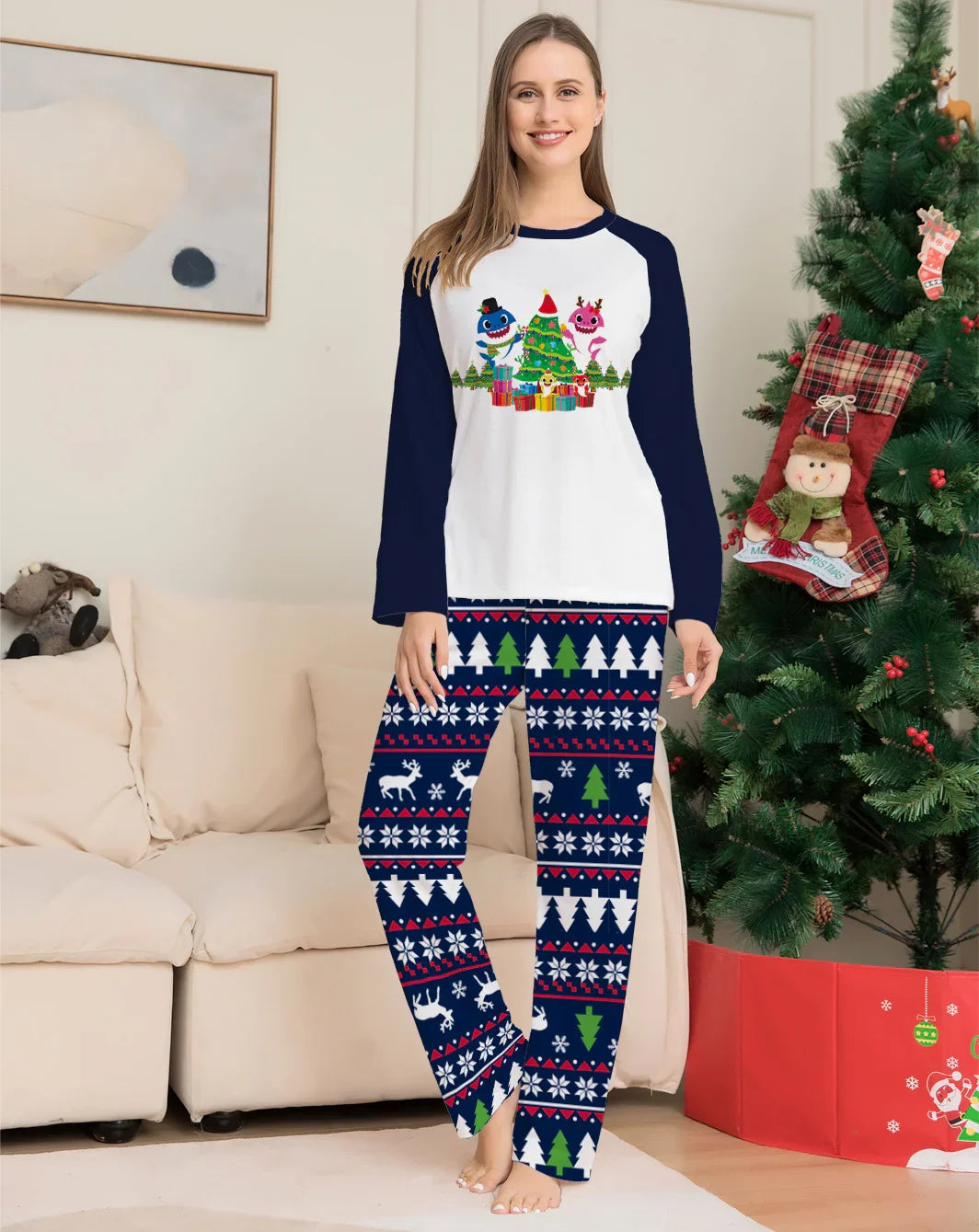 Woman wearing festive Christmas pajamas with holiday tree, gifts, and reindeer patterns next to decorated Christmas tree