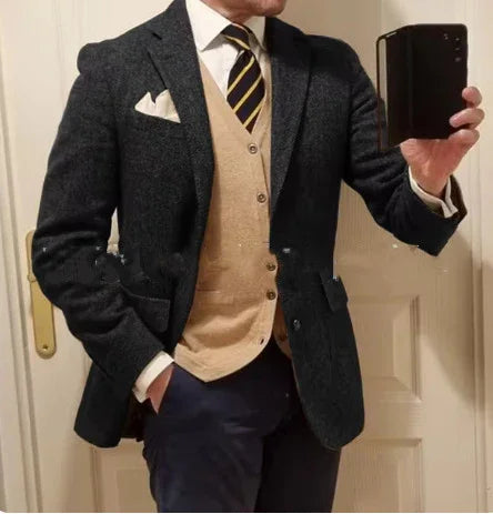 man wearing dark gray blazer, beige cardigan, white shirt, and striped tie taking mirror selfie indoors