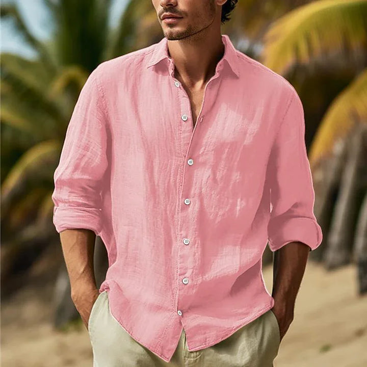 Man wearing light pink linen shirt with rolled sleeves and beige pants on a tropical beach