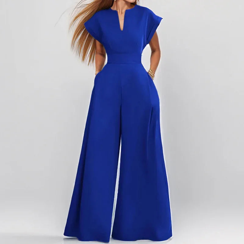 Woman wearing royal blue wide-leg jumpsuit with cap sleeves and V-neck on grey background