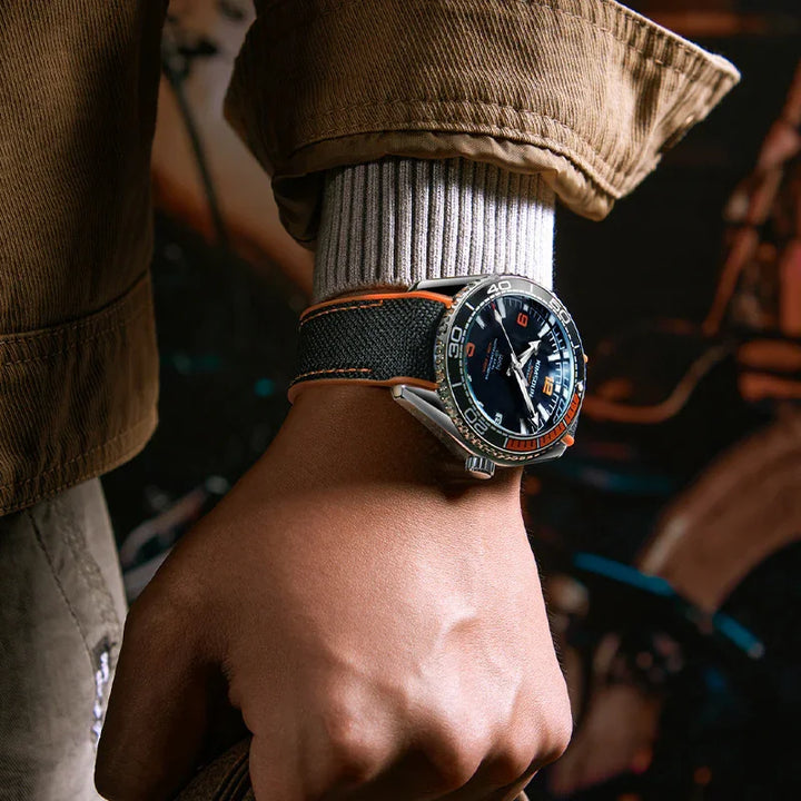 Close-up of wrist wearing luxury diver watch with black and orange bezel and fabric strap