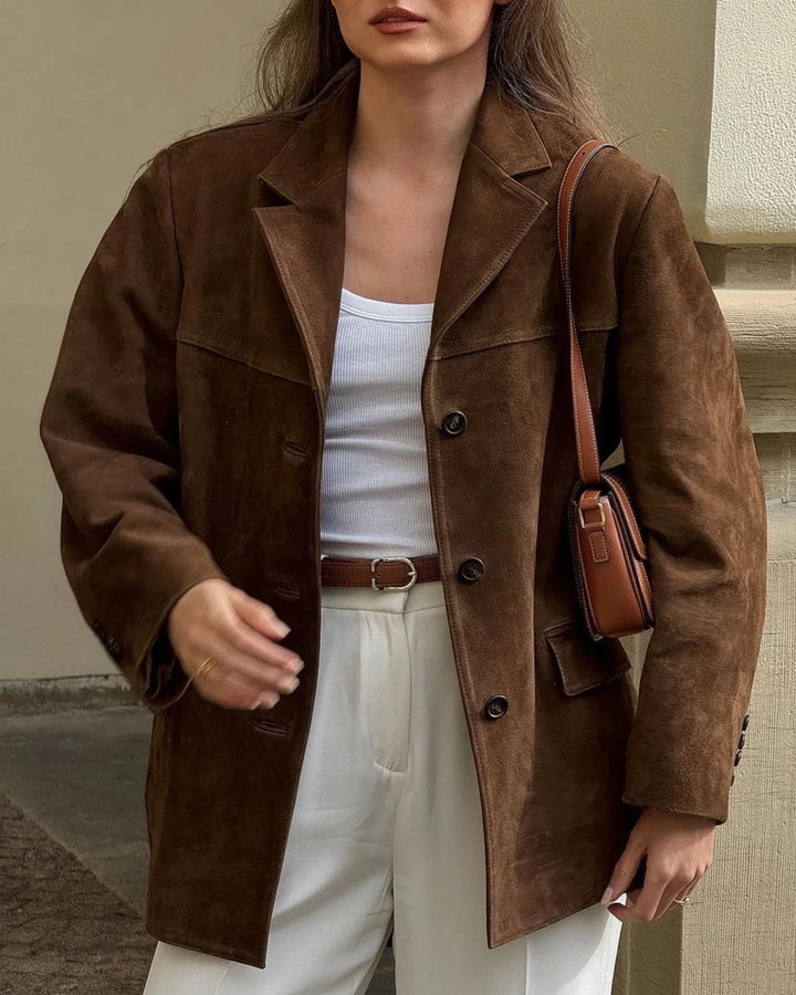 Woman wearing oversized brown suede jacket with white tank top, cream pants, and brown leather shoulder bag