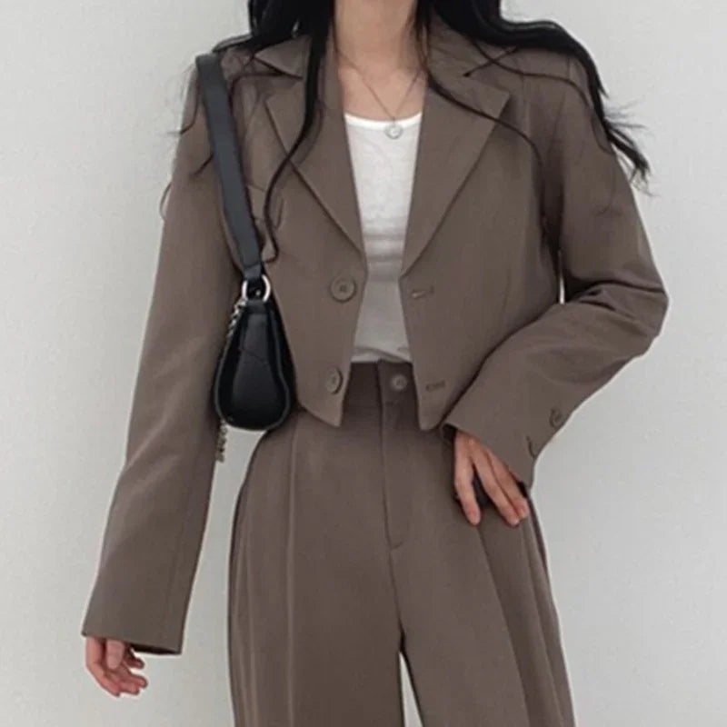 Woman wearing brown cropped blazer and high-waisted pants with white top and black shoulder bag