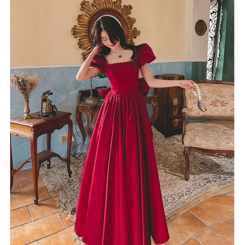 Woman in elegant red gown with puff sleeves and pearl necklace in vintage room