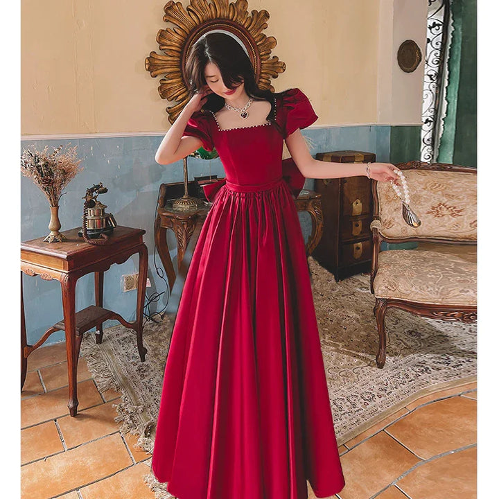 Woman in elegant red gown with puff sleeves and pearl necklace in vintage room