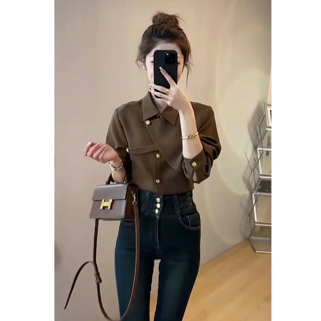 Woman in brown button-up shirt and high-waisted dark jeans taking mirror selfie with brown handbag