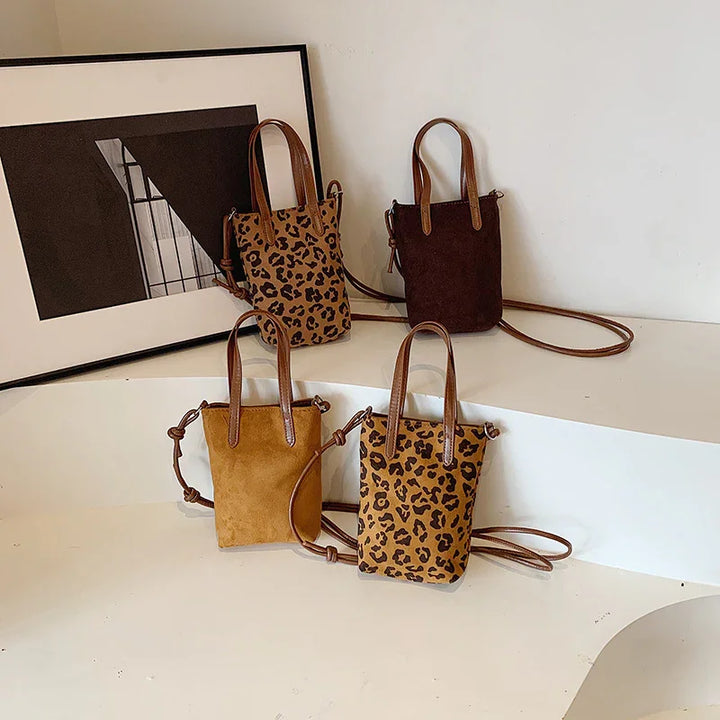Four small leather and suede handbags with leopard print and solid colors displayed on white curved shelves