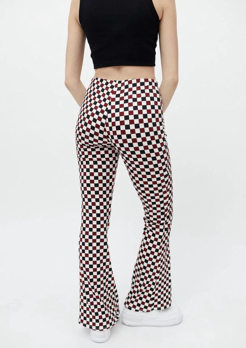 Woman wearing high-waisted, black, white, and red checkered flare pants with white sneakers and black crop top
