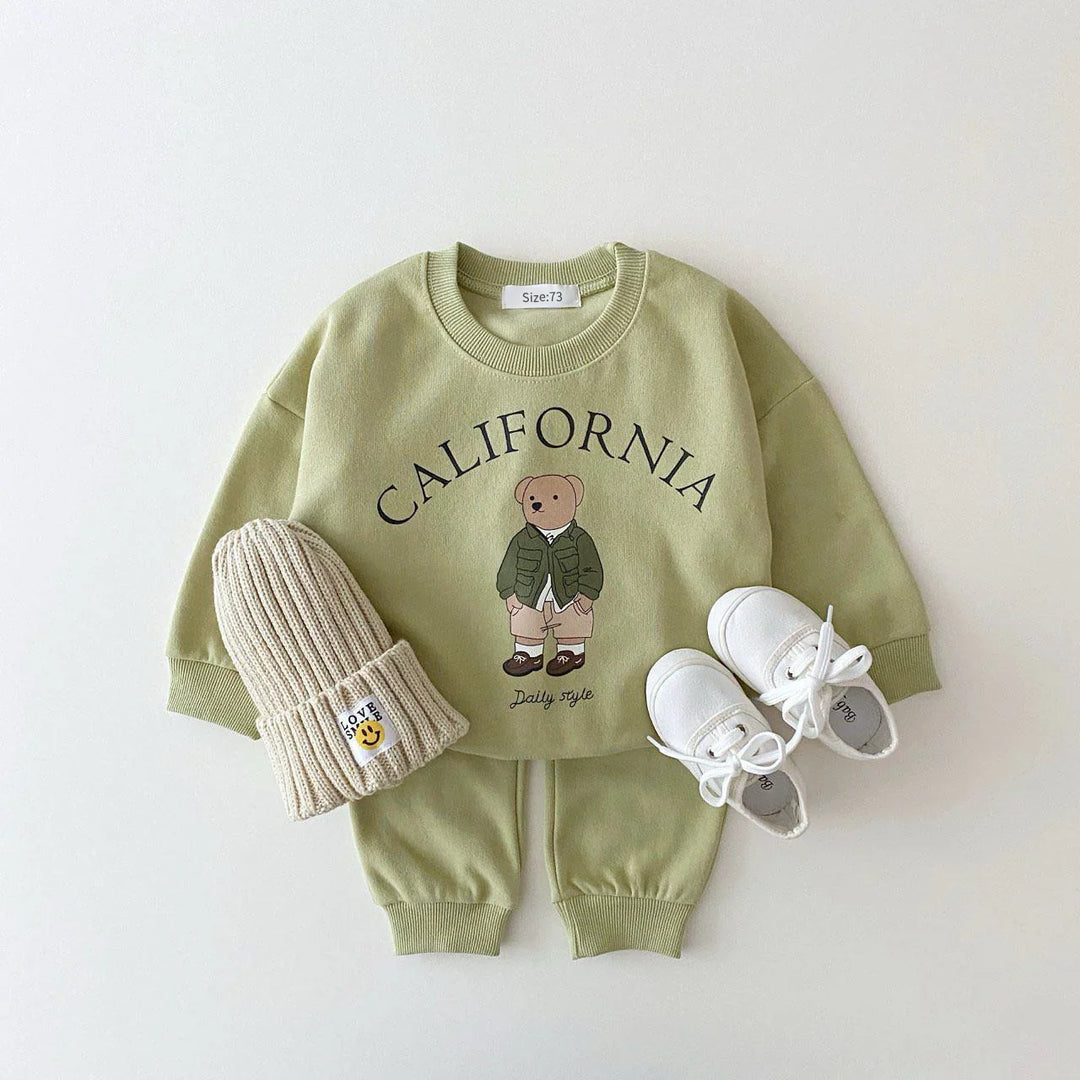 Green toddler outfit with California bear print, beige knit hat, and white shoes on white background