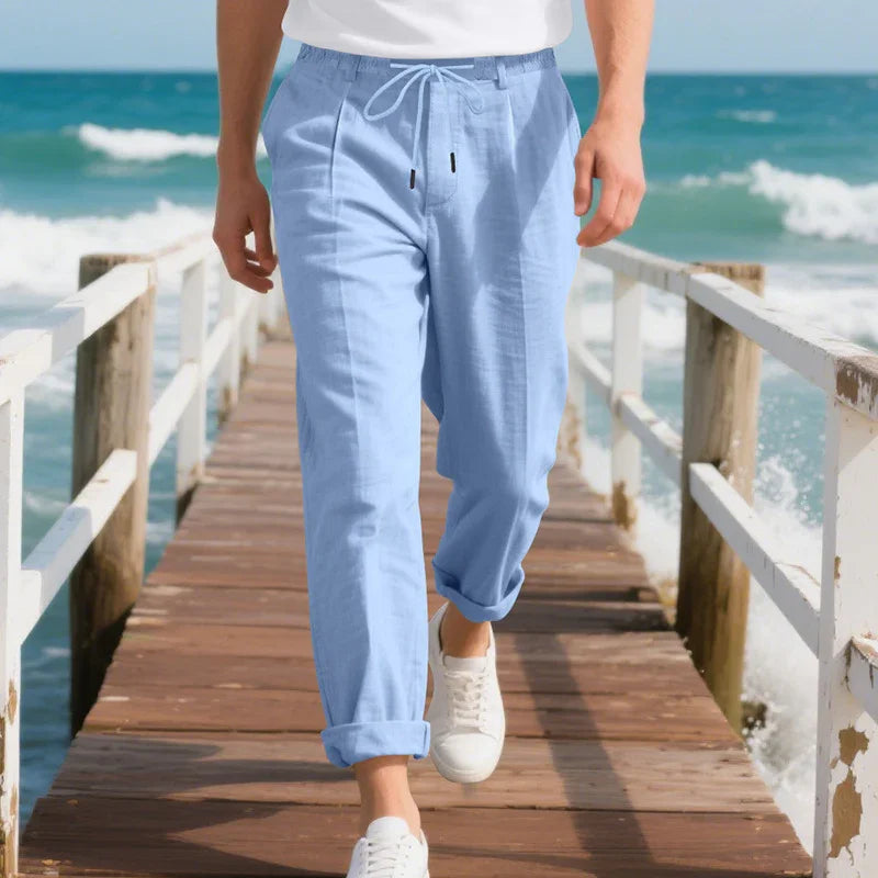 Close-up of man wearing light blue drawstring pants and white sneakers walking on wooden pier by the sea