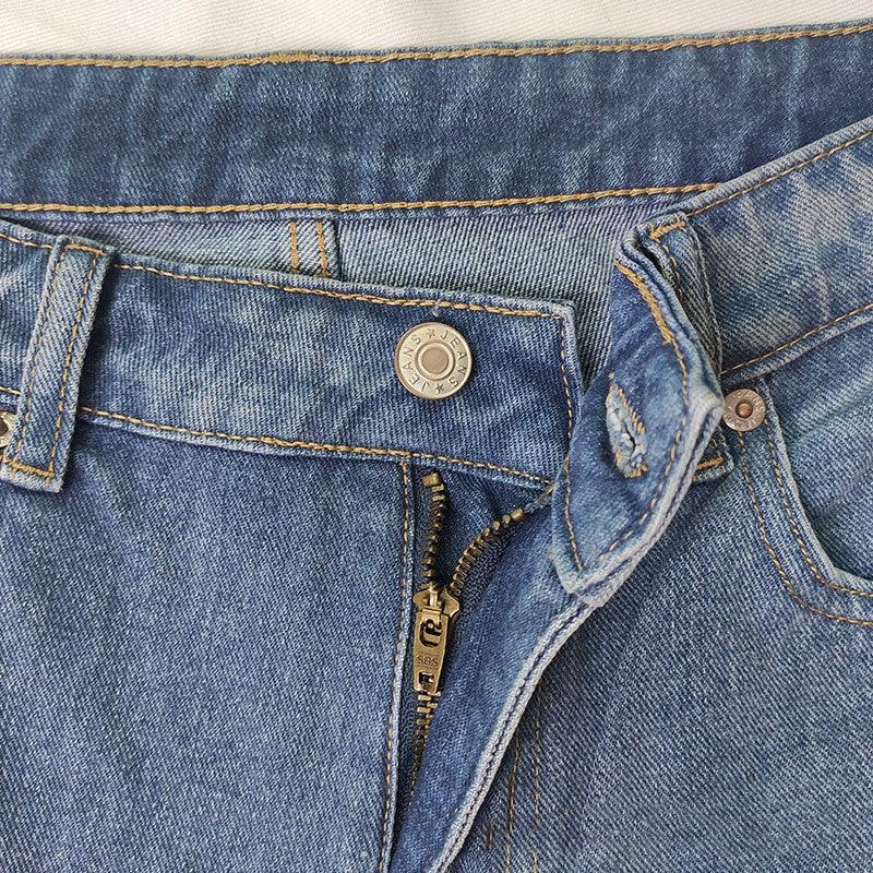 Close-up of blue denim jeans waistband with partially open zipper and metal button