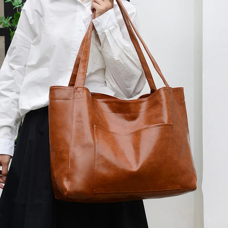Woman holding large brown leather tote bag with front pocket, wearing white shirt and black skirt
