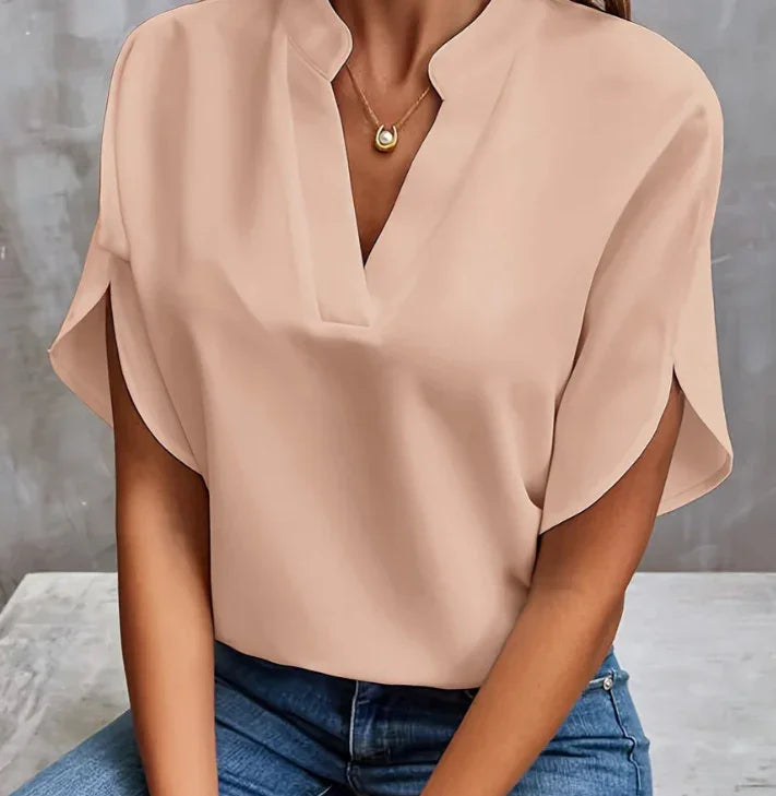 Woman wearing beige loose short sleeve blouse with V-neck and gold necklace, paired with blue jeans