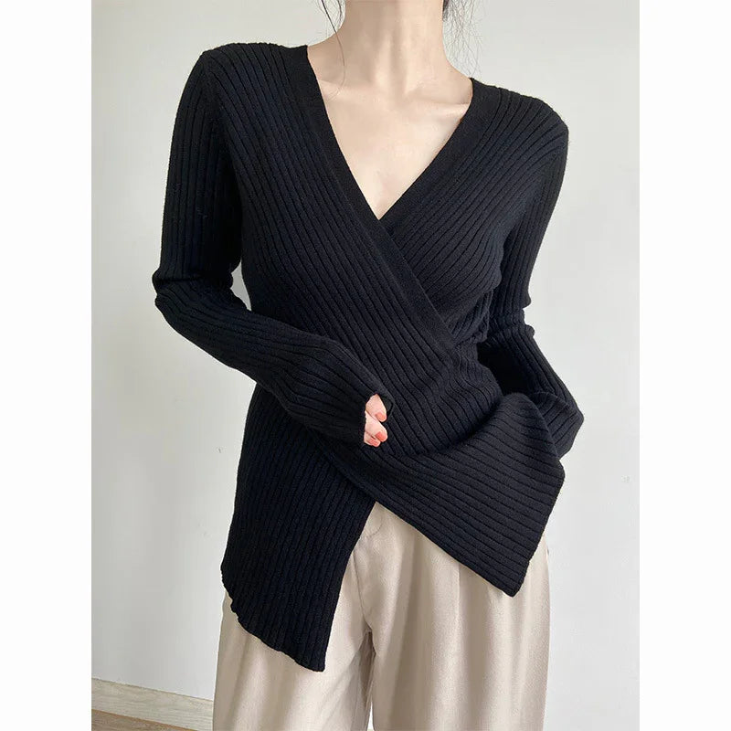 Woman wearing black ribbed knit wrap sweater with V-neck and beige trousers against plain background