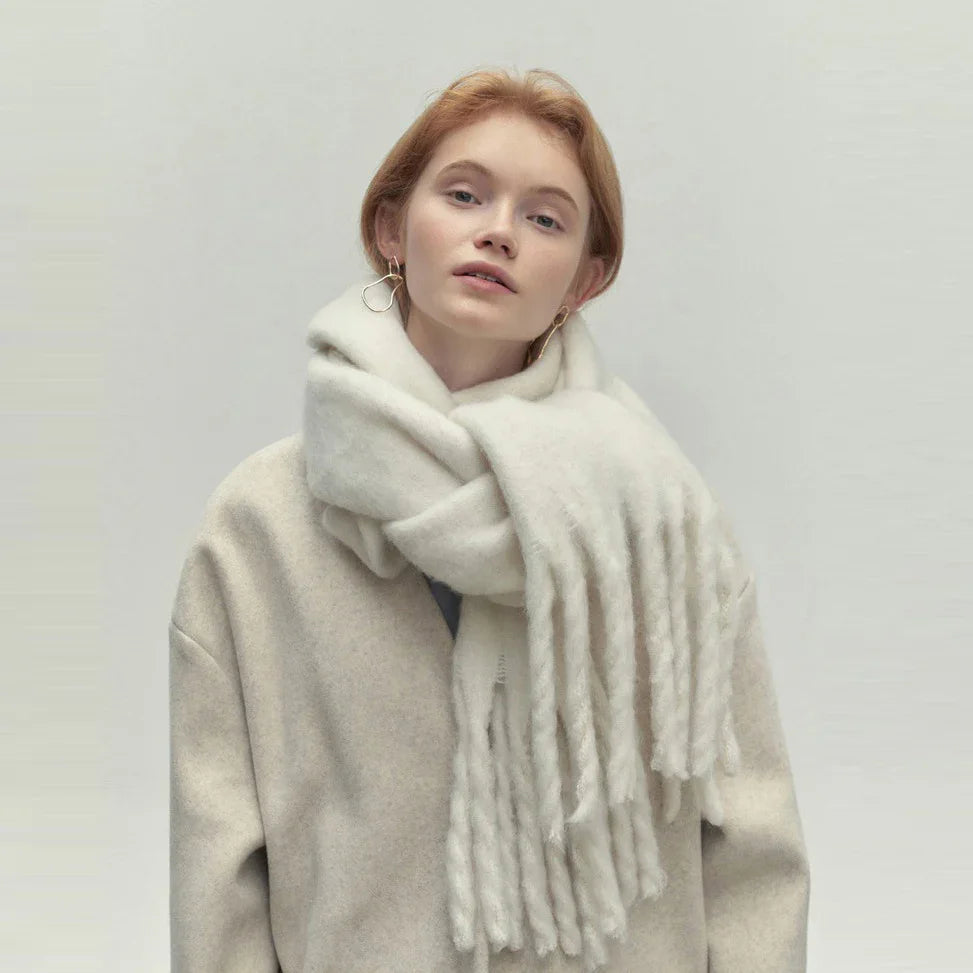 Young woman wearing oversized beige coat and thick white fringed scarf on gray background