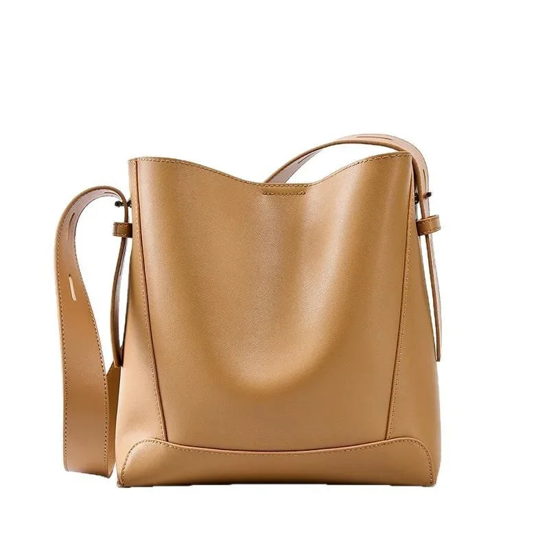 tan leather bucket bag with adjustable strap and minimalist design on white background