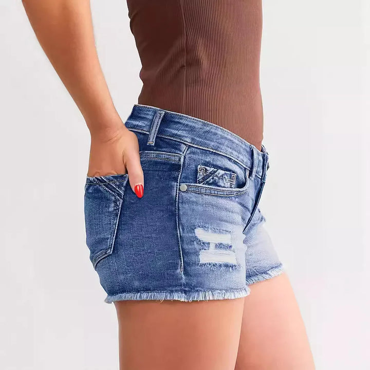 Close-up of woman wearing distressed denim shorts and brown ribbed top with hand in pocket