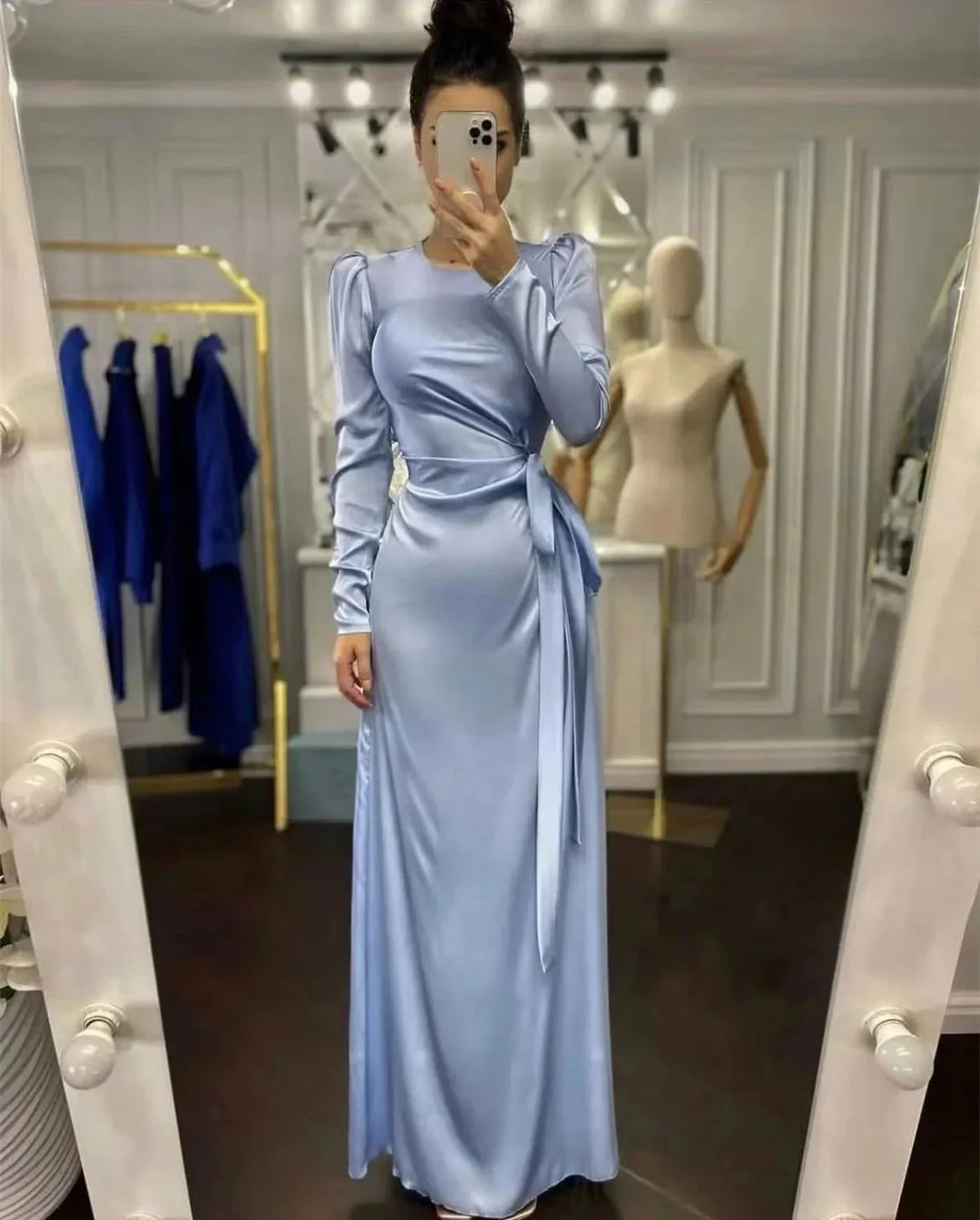 Woman in a light blue satin long dress with puff sleeves posing in a boutique fitting room