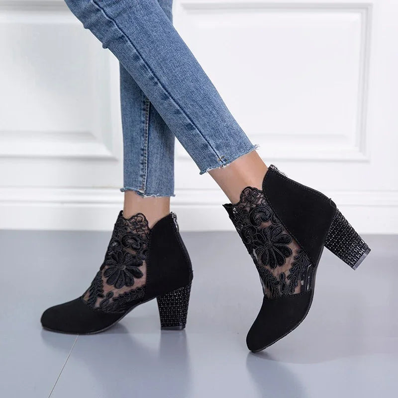 Black high-heeled ankle boots with floral lace design worn with cropped blue jeans on gray floor