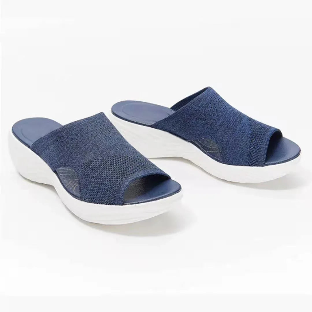 Pair of navy blue knit slip-on wedge sandals with white textured soles on white background
