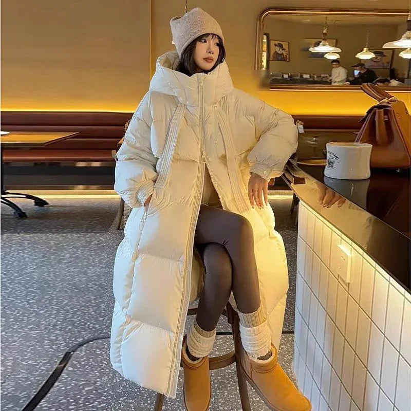 Woman in long white puffer coat, beige knit hat, and tan boots sitting on stool in cozy café