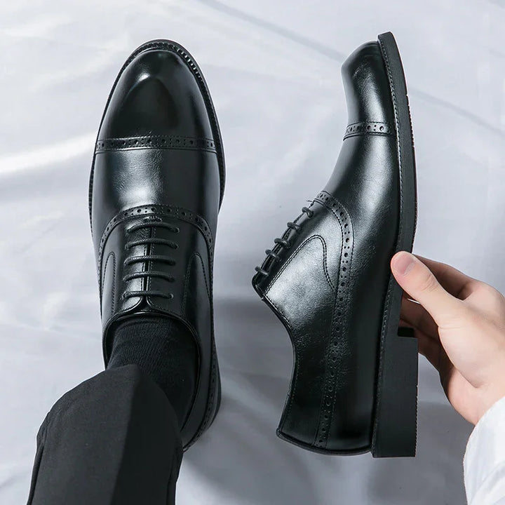 Black leather men's dress shoes with brogue detailing on white background, one worn and one held