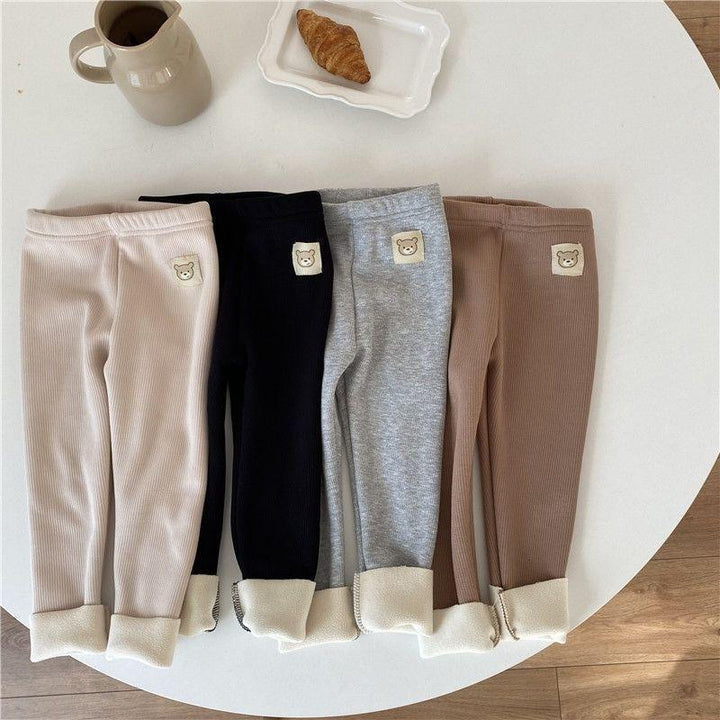 Four pairs of ribbed fleece-lined toddler leggings in beige, black, grey, and brown with bear patch on white table with croissant and beige jug