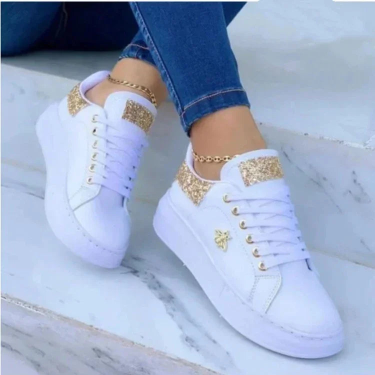 White platform sneakers with gold glitter details and bee emblem worn with blue jeans on marble steps