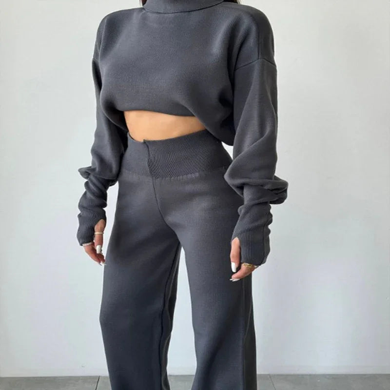 Woman wearing dark gray cropped long-sleeve sweater and matching high-waisted wide-leg pants against white wall