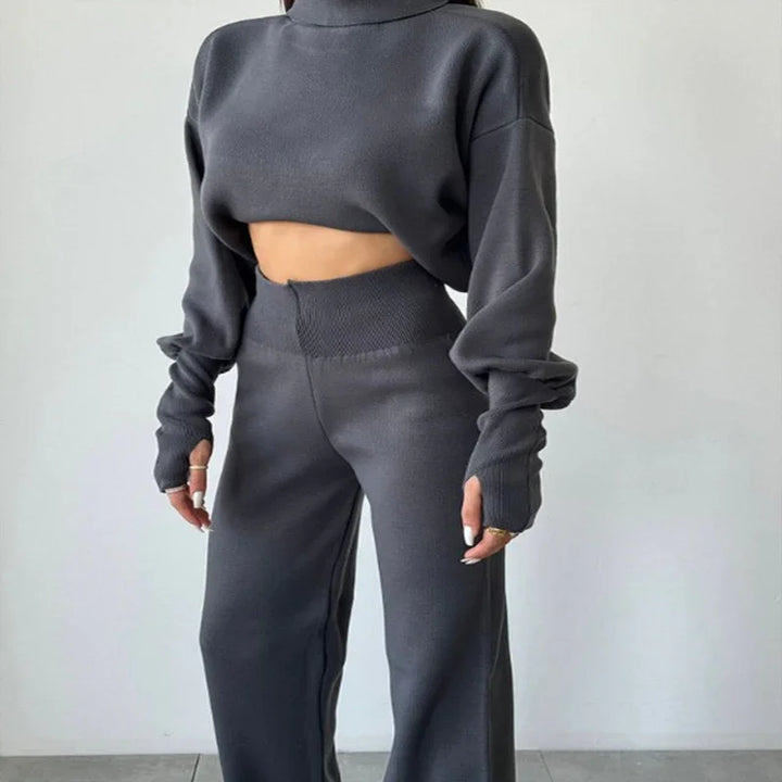 Woman wearing dark gray cropped long-sleeve sweater and matching high-waisted wide-leg pants against white wall