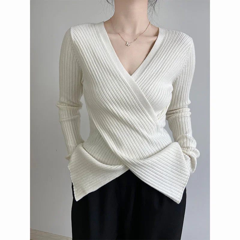 Woman wearing white ribbed knit wrap sweater with long sleeves and V-neck, paired with black pants