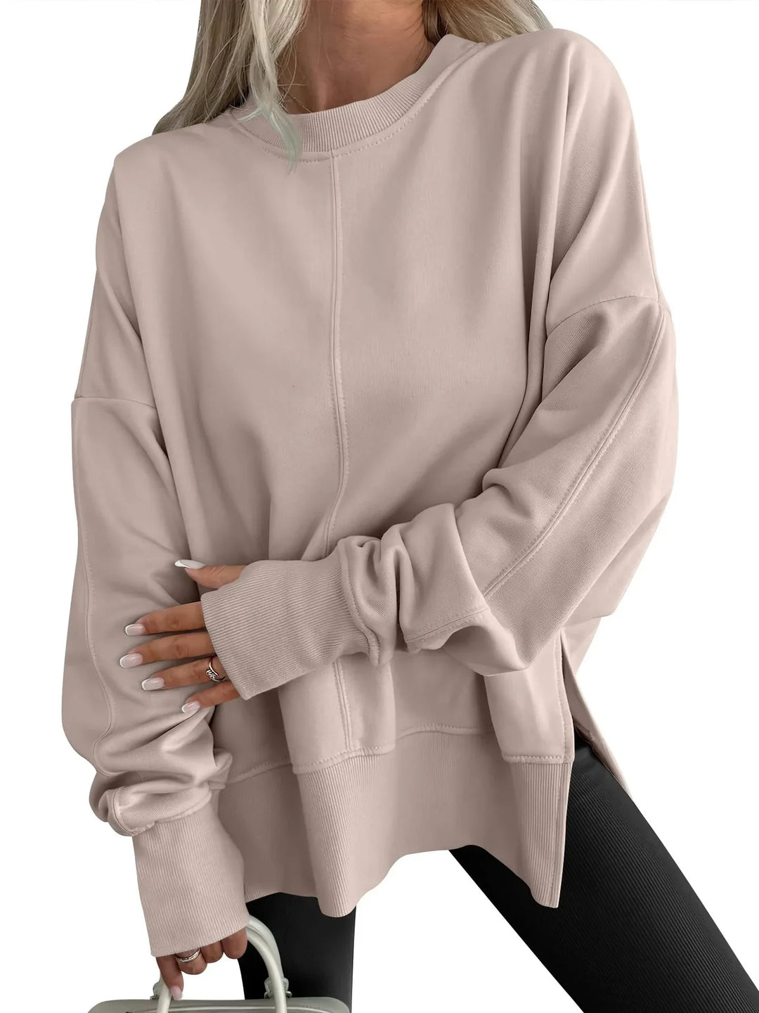 Woman wearing loose beige sweatshirt with ribbed cuffs and side slits, paired with black leggings