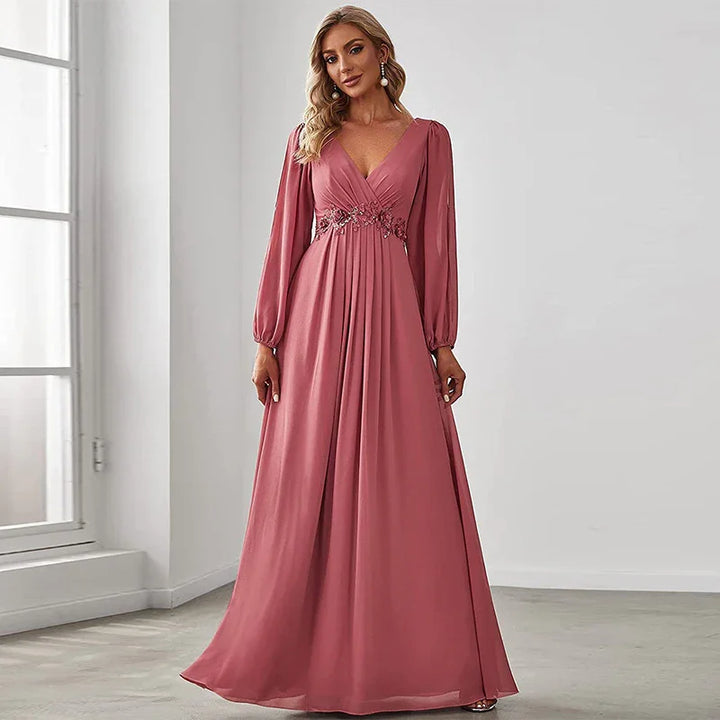 Woman wearing a long-sleeve dusty rose formal gown with V-neck and floral waist embellishment in bright room