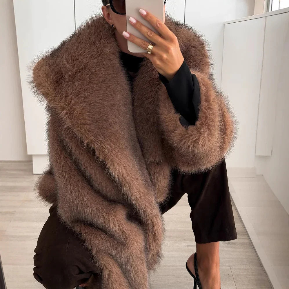 Woman in oversized brown faux fur coat, black pants, and high heels taking a mirror selfie indoors