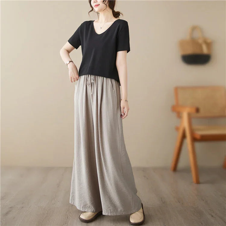 Woman wearing loose beige wide-leg pants and black short-sleeve top in a minimal indoor setting