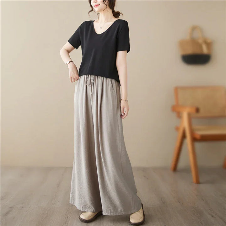 Woman wearing loose beige wide-leg pants and black short-sleeve top in a minimal indoor setting