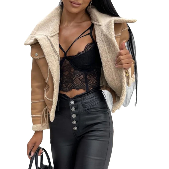 Woman wearing tan shearling jacket, black lace crop top, and high-waisted black leather pants holding a handbag