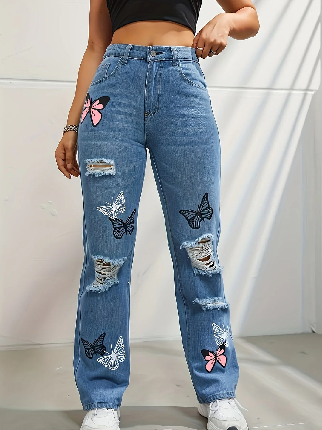Woman wearing high-waisted ripped blue jeans with white, black, and pink butterfly prints