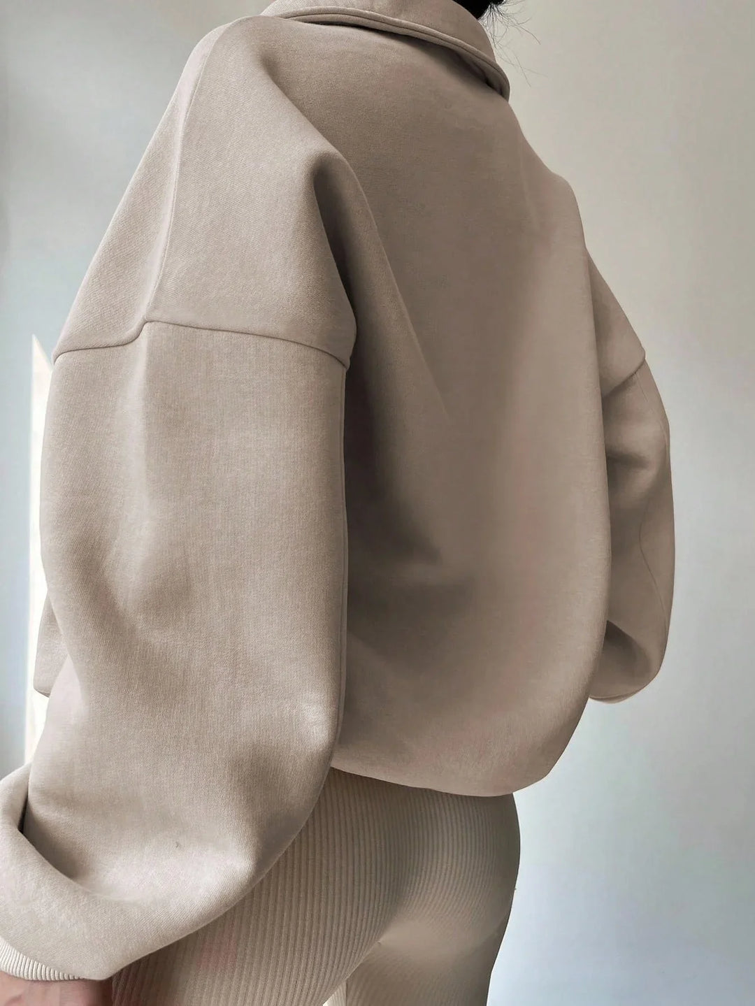 Close-up of a person wearing an oversized beige sweatshirt and beige ribbed pants against a plain background